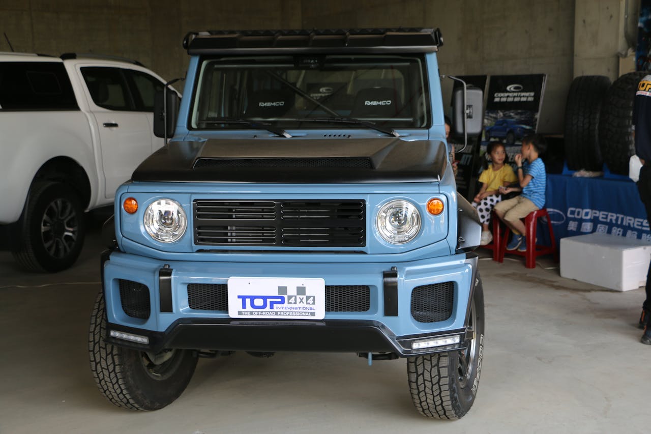Blue off-road vehicle displayed indoors in Taiwan with people in the background.
