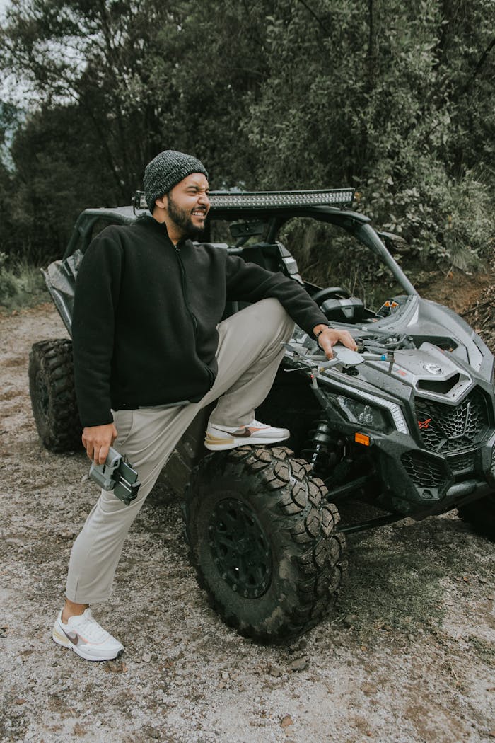 A man leaning on an off-road vehicle in a lush green forest.